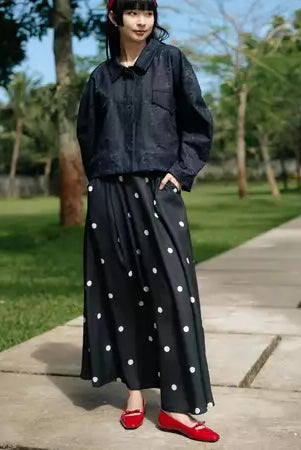 Person wearing a black jacket and polka dot skirt by Haidee Orlin with red shoes in a park.