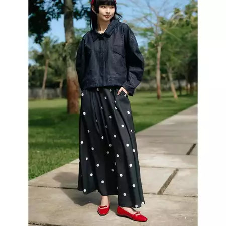 Person wearing a black jacket and polka dot skirt by Haidee Orlin with red shoes in a park.