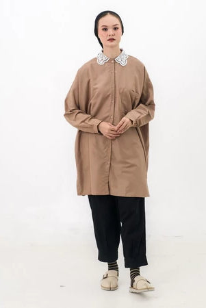 A woman wearing a brown tunic with long sleeves and a round neckline, paired with black trousers and light-colored shoes.