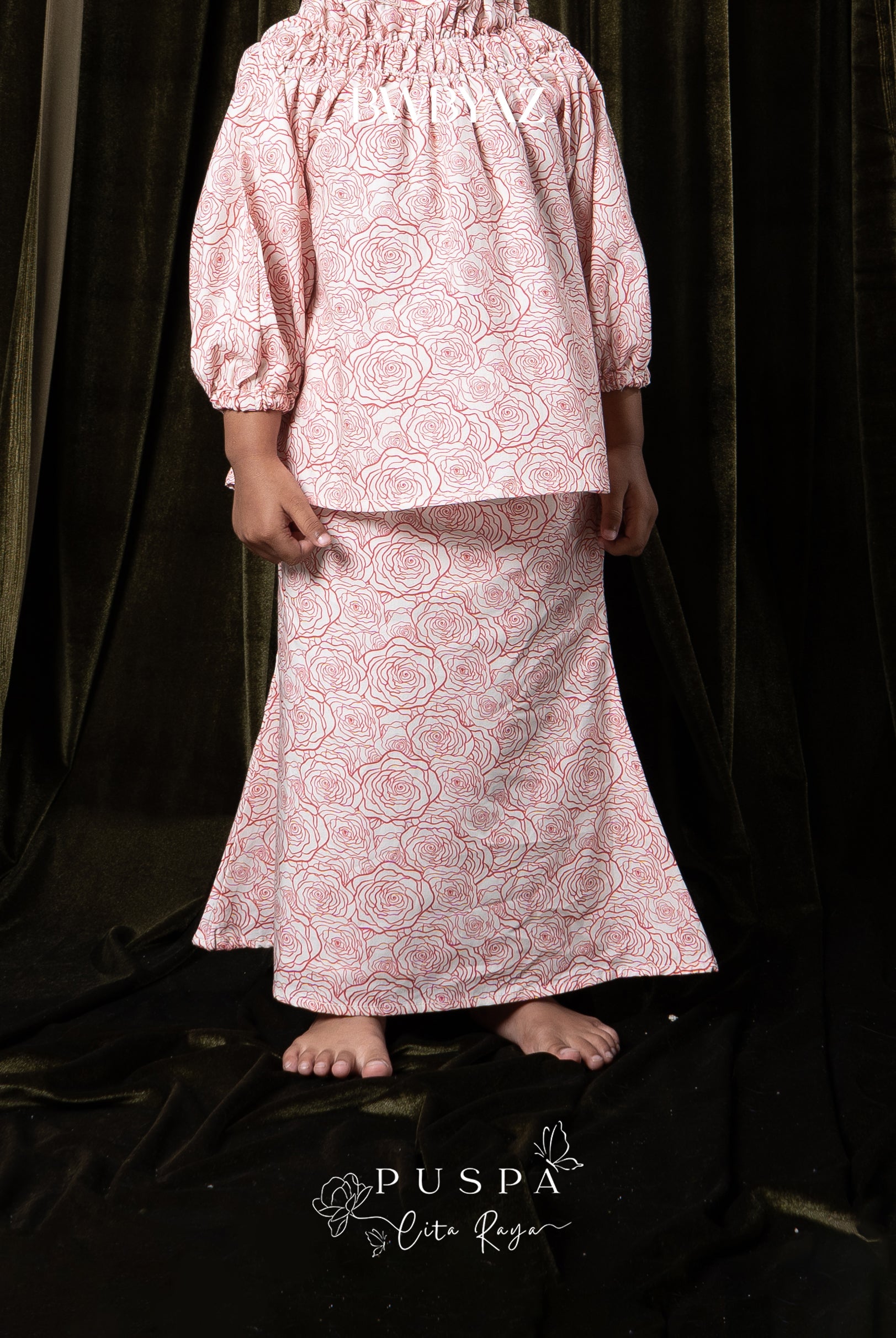 Person wearing a pink patterned top and skirt by BWBYAZ against a dark curtain.