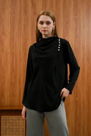 Woman wearing a black Rachel Blouse by Kasa Heritage with pearl details against a wooden background