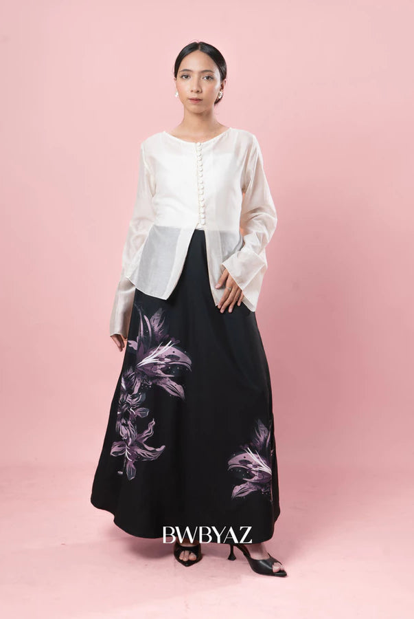 Woman wearing a white top and black skirt with floral design on a pink background, featuring the brand BWBYAZ.