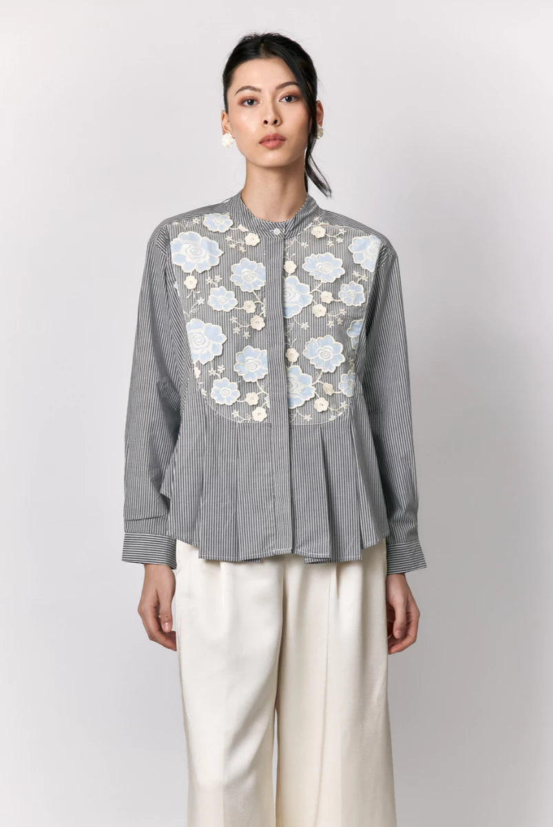 Woman wearing a gray striped shirt by Studio Tui with floral embroidery on a white background