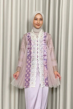 A woman wearing a traditional Kebaya Heather dress by Kartinis Label with batik and lace decorations, featuring a silhouette commonly associated with casual to elegant attire.