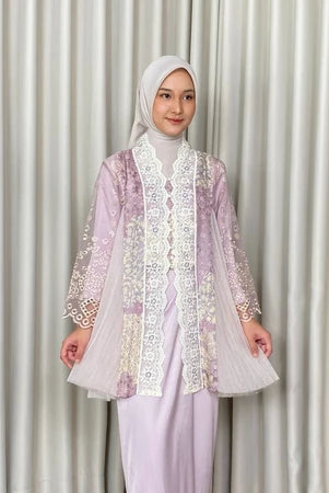A woman wearing a lavender Kartinis Label Raline Kebaya, featuring batik patterns and lace embellishments.