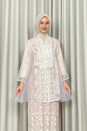 A woman modeling a white Kartinis Label kebaya, featuring batik and lace details, with a silhouette of a traditional kebaya dress.
