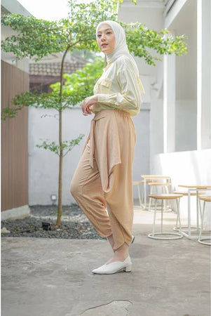 A woman standing in an outdoor setting wearing beige pants by Abame and a matching top.
