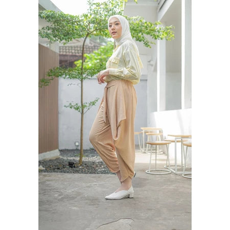 A woman standing in an outdoor setting wearing beige pants by Abame and a matching top.