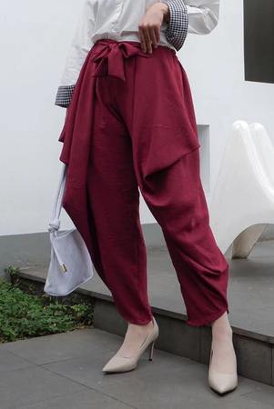 A woman standing in an outdoor setting wearing maroon rami pants by Abame and a white top.