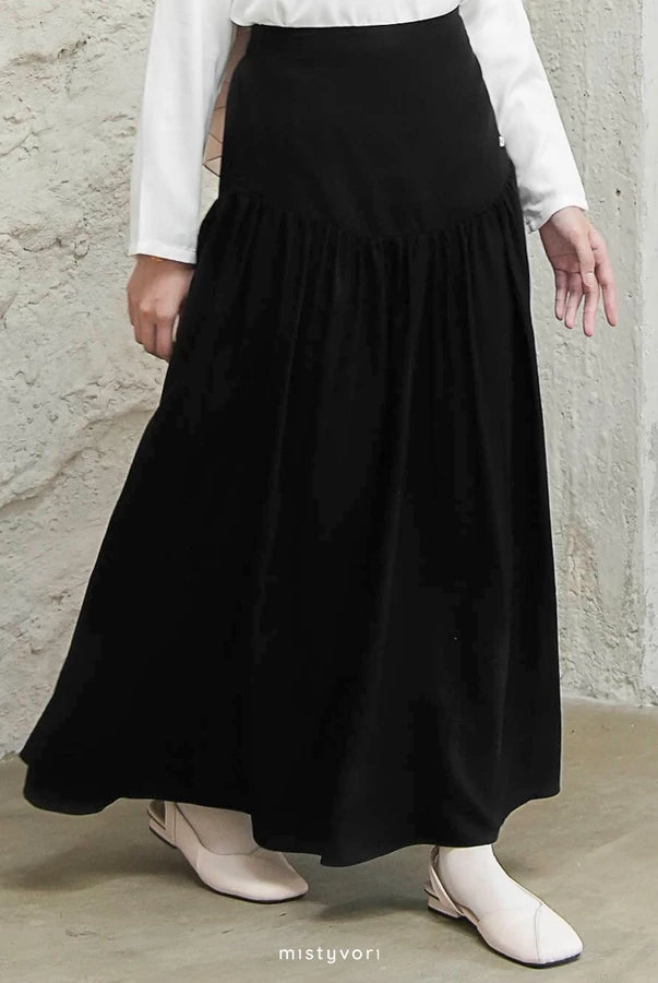Person wearing a black skirt by Mistyvori and white top against a concrete wall.
