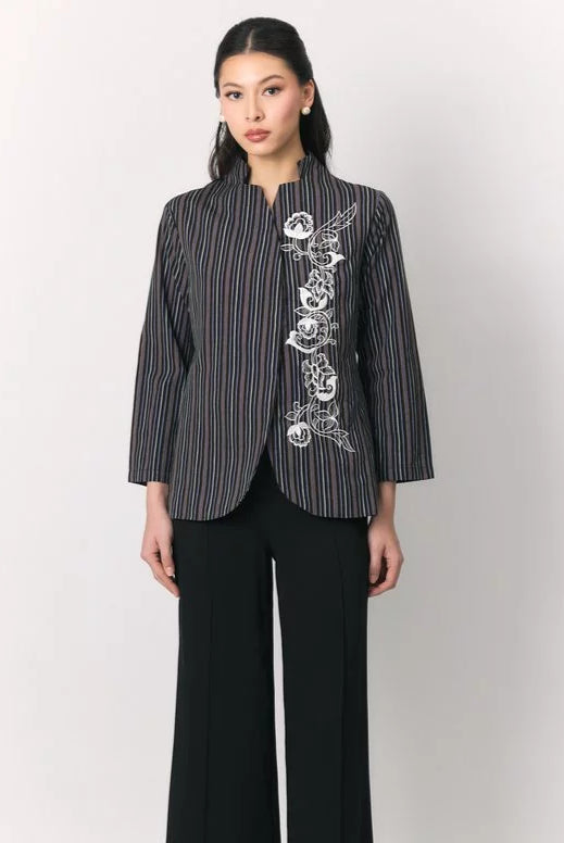 A woman modeling a black three-quarter sleeve top by Studio Tui with vertical red and white stripes and white floral embroidery on the front, paired with black wide-leg trousers, against a light gray studio background.