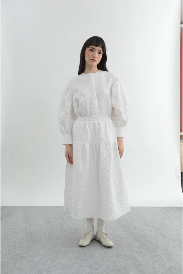 Person wearing a white top and patterned long white skirt by Yestoday on a gray background
