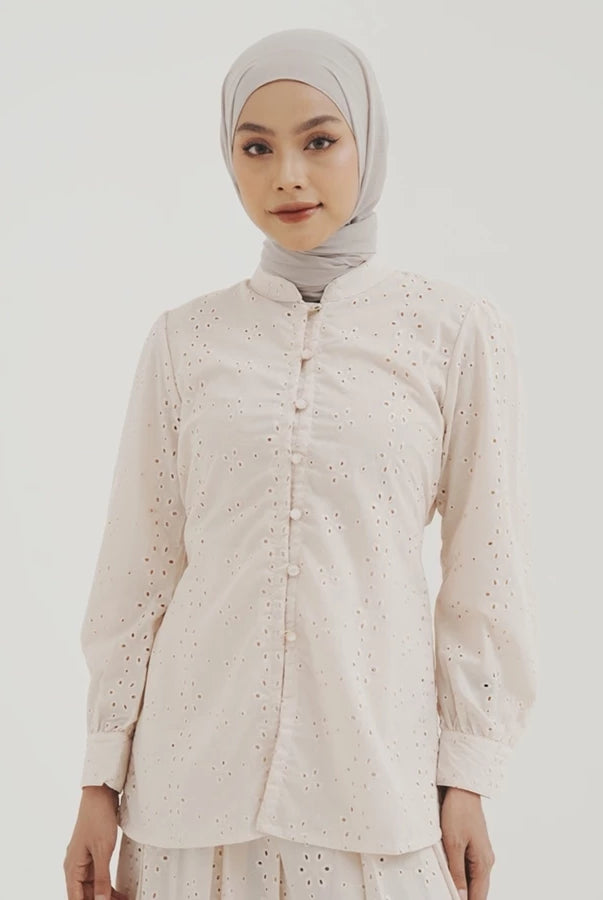 Woman wearing a light-colored blouse by Tunique with intricate patterns on a plain background
