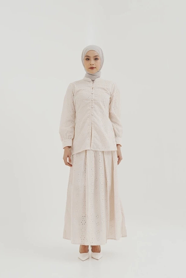 Person wearing a light-colored patterened skirt by Tunique with a hijab on a white background