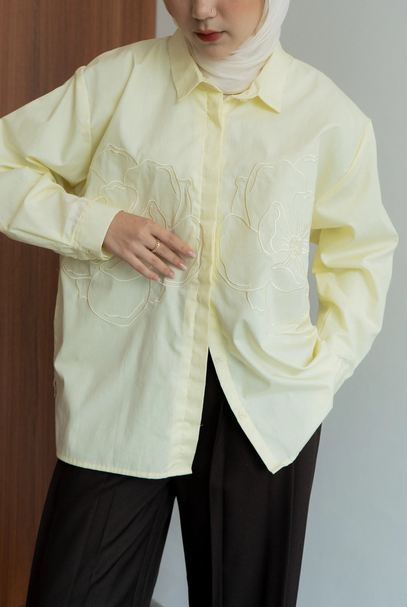 Person wearing a light yellow shirt with floral embriodered patterns from BWBYAZ against a plain background