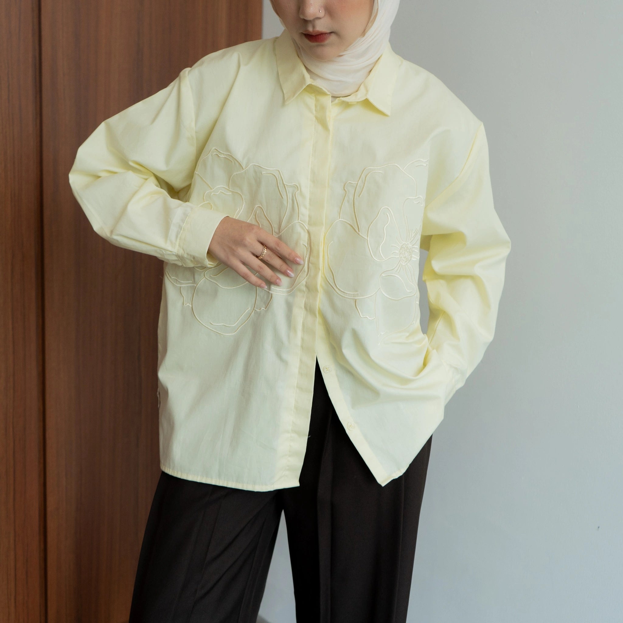 Person wearing a light yellow shirt with floral embriodered patterns from BWBYAZ against a plain background