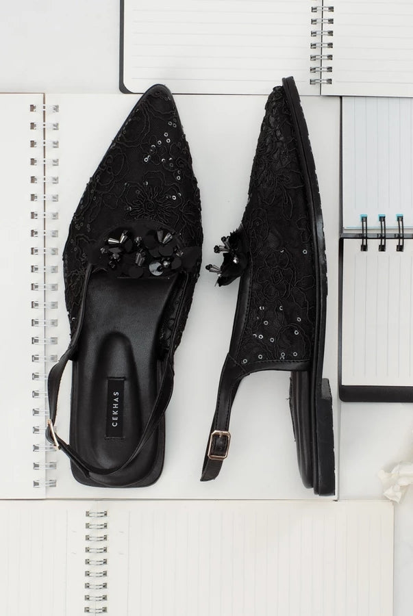 Black studded sandals by Cekhas on a white surface with a notebook and flower.
