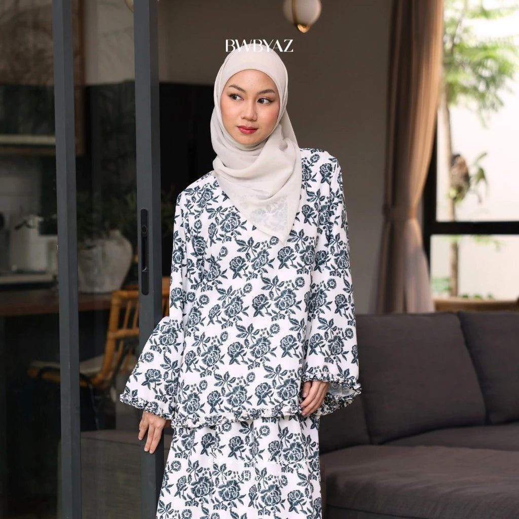 A woman wearing a white and blue floral ruffle top with long sleeves from BWBYAZ and a headscarf.
