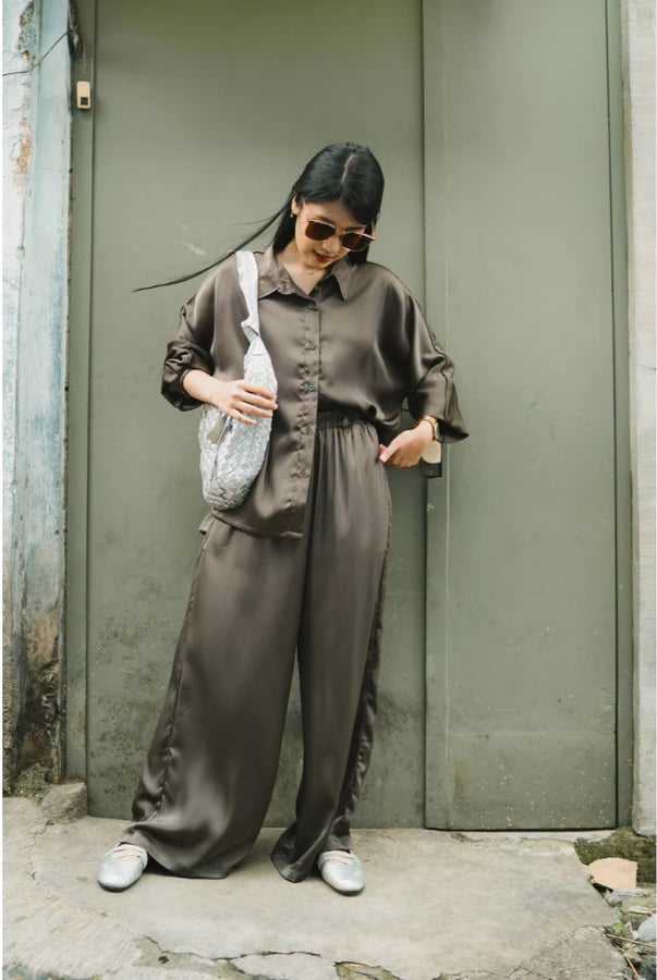 Woman in a brown top and culottes standing against a green wall.
Seorang wanita mengenakan atasan cokelat dan celana kulot sedang berdiri di depan dinding hijau.