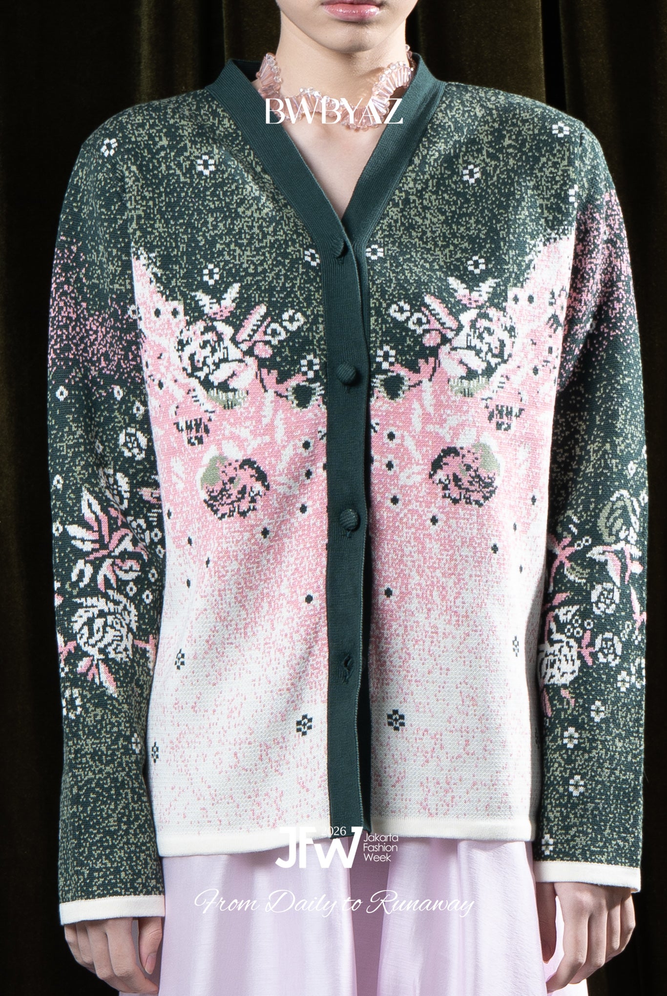 Person wearing a green cardigan with pink and white floral pattern by BWBYAZ with a dark background