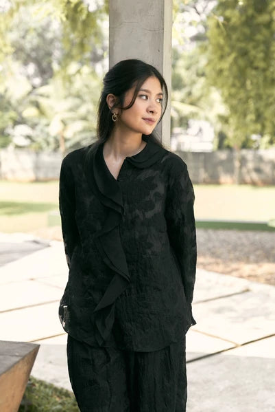 Woman in a black shirt with floral detail by Studio Tui standing outdoors with greenery in the background