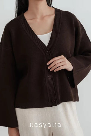Person wearing a dark brown cardigan over a white shirt with a plain background, featuring the brand 'kasyalia'.