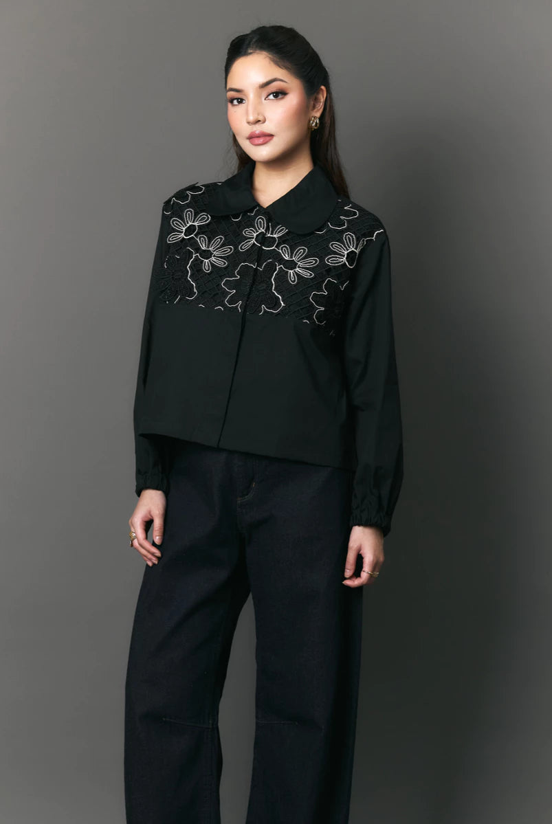 Woman wearing a black shirt with floral embroidery by Studio Tui against a gray background
