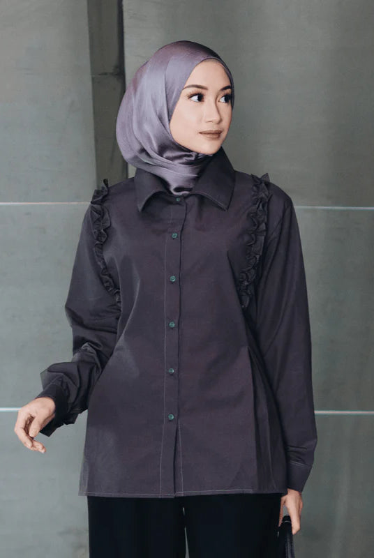 Woman wearing a dark brown blouse with ruffled sleeves from Atala Scarves against a gray wall