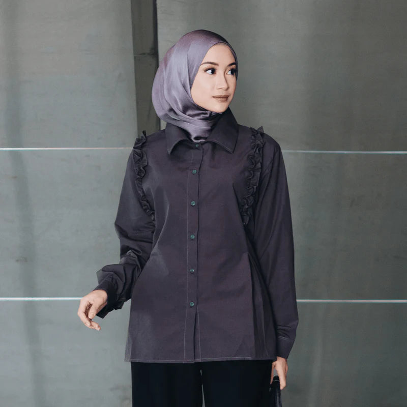 Woman wearing a dark brown blouse with ruffled sleeves from Atala Scarves against a gray wall