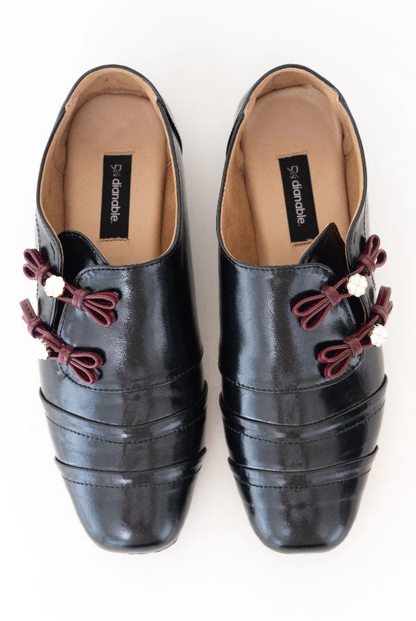 Black flatshoes with red decorative bows by Dianable on a white background
Flat shoes wanita hitam dengan pita hias merah karya Dianable di atas latar belakang putih