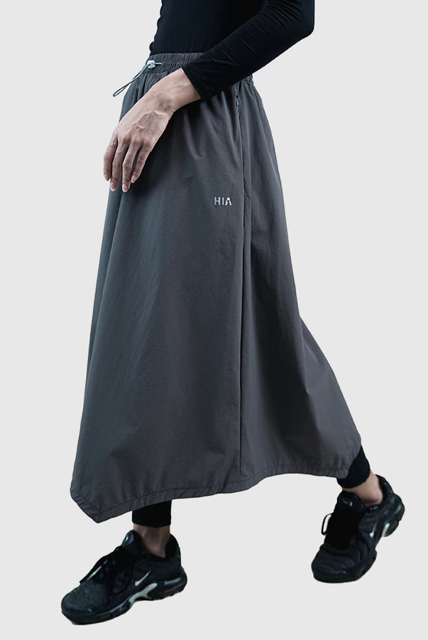 Person wearing a long dark gray skirt with 'HIA' branding on a light gray background