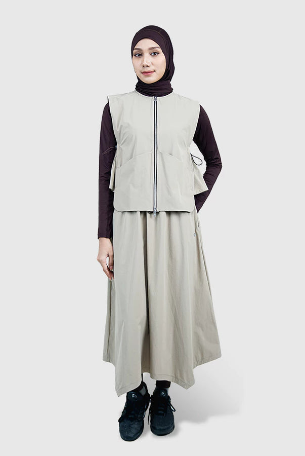 Person wearing a beige vest by HIA and long skirt with a black hijab on a white background