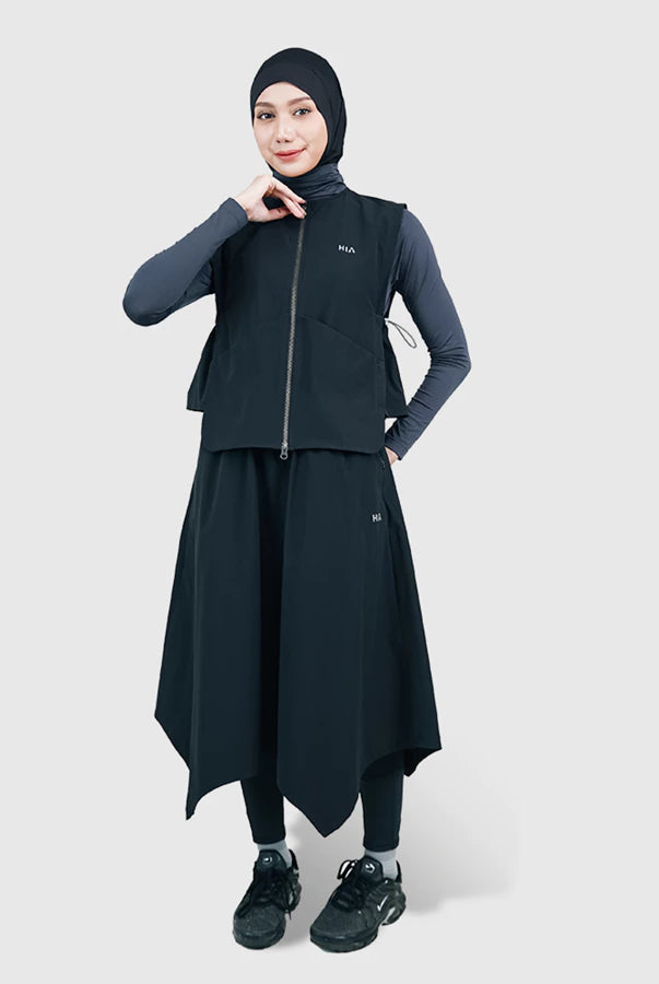 Woman wearing a black vest by HIA with a hijab on a white background