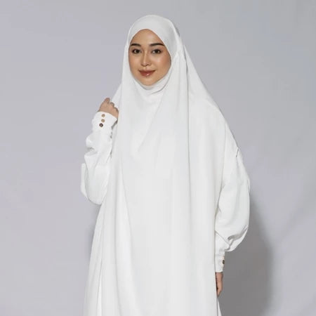 Woman wearing a white hijab khimar by Lozy Hijab and white outfit against a gray background