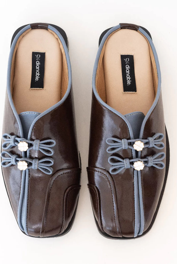 Pair of brown mules flats by Dianable with decorative elements on a white background