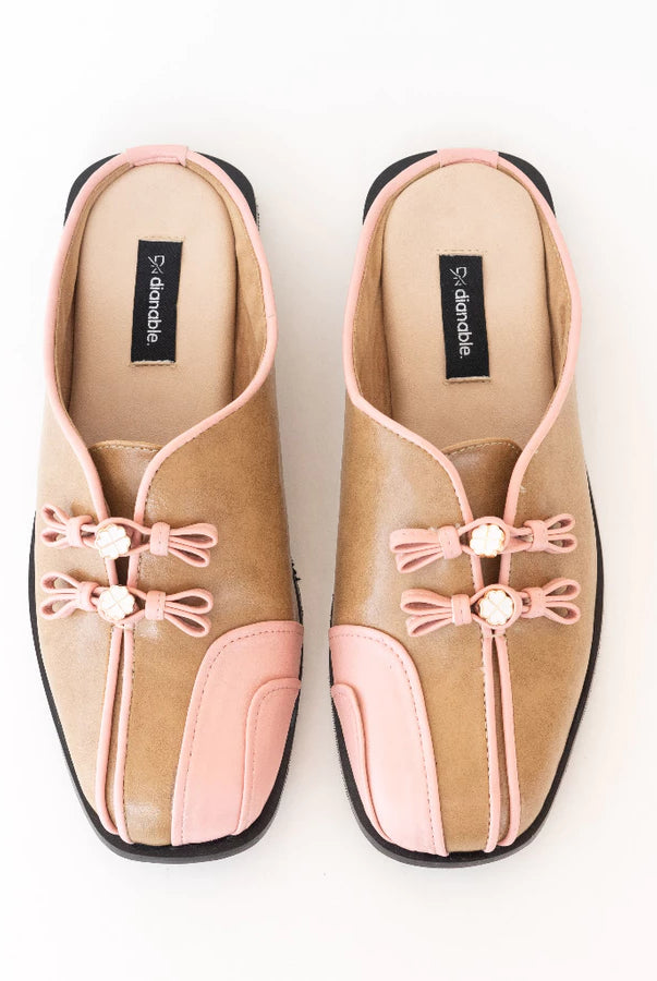 Pair of tan and pink mules flats by Dianable with decorative bows on a white background
