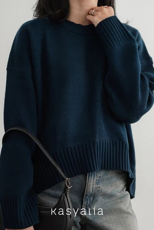 Person wearing a dark blue oversized sweater with a plain background, featuring the brand 'kasyalia'.