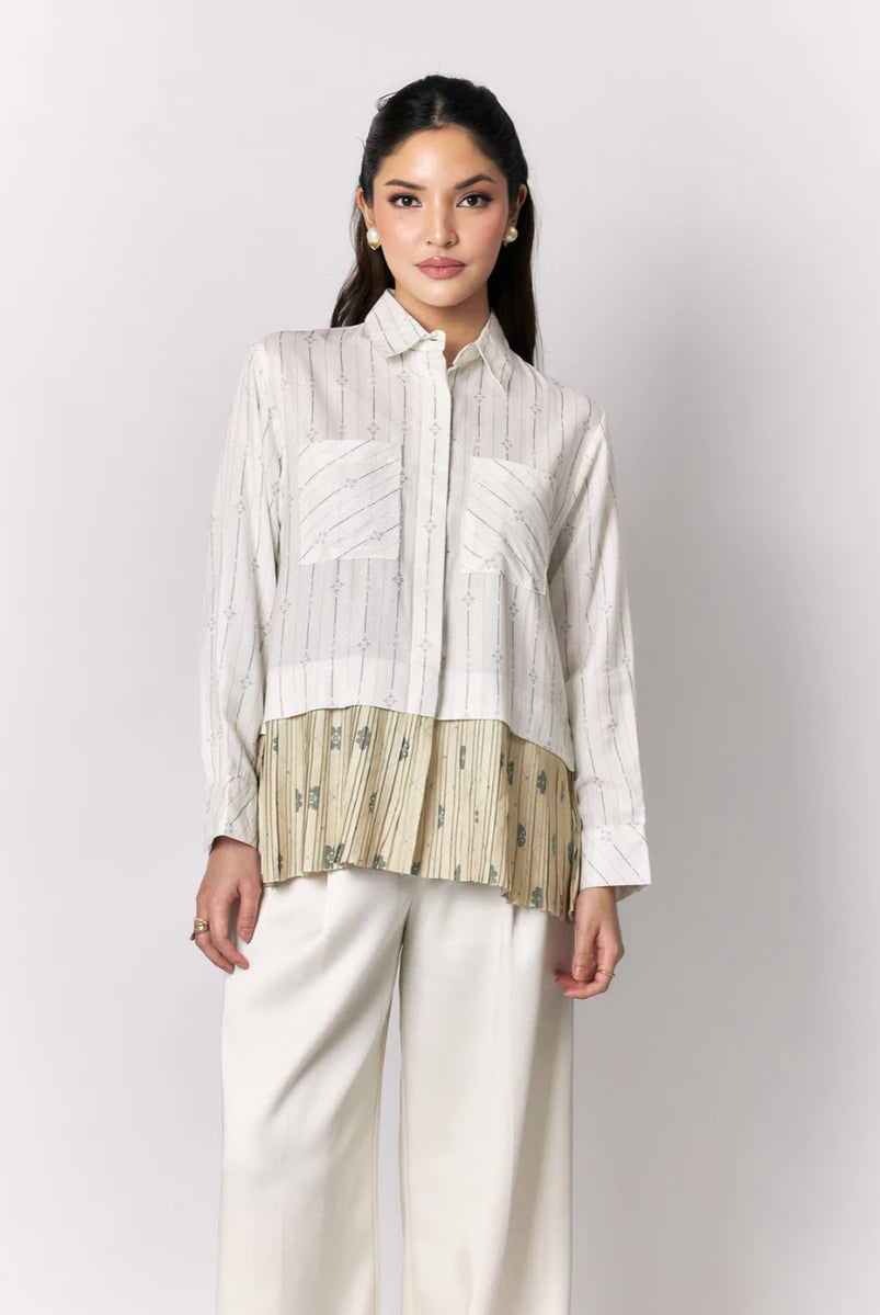 Woman wearing a white shirt with a textured green panel by Studio Tui and white pants on a light gray background