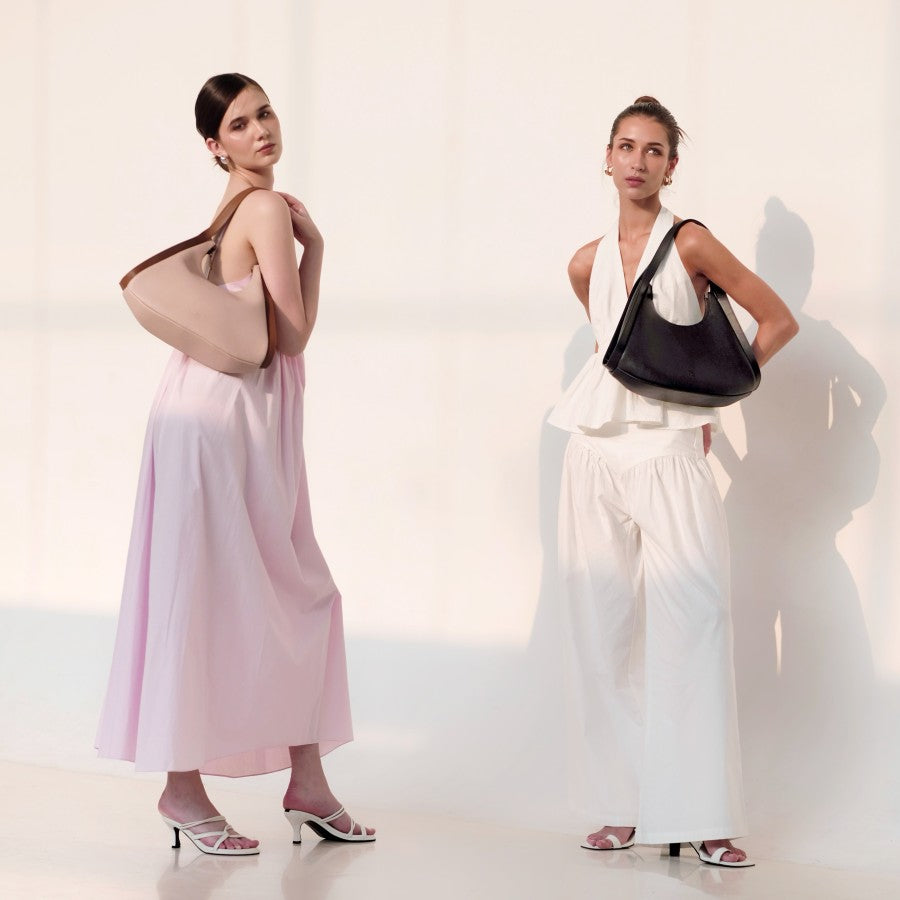 Two women in dresses and sandals pose together, showcasing their fashionable bags from purotti.