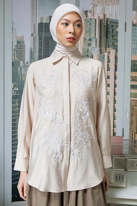 Woman wearing a beige embroidered shirt by Hijabchic with a cityscape in the background
