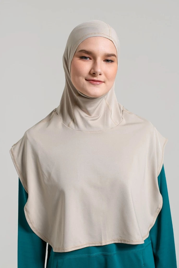 Woman wearing a beige sport hijab by Noore and teal top against a light gray background