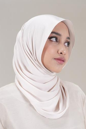 Woman wearing a light pink pashmina hijab by Tantri Namirah Official against a plain background