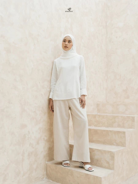 Woman wearing a white top and light brown wide-leg pants by Swifter with a hijab standing on a staircase.