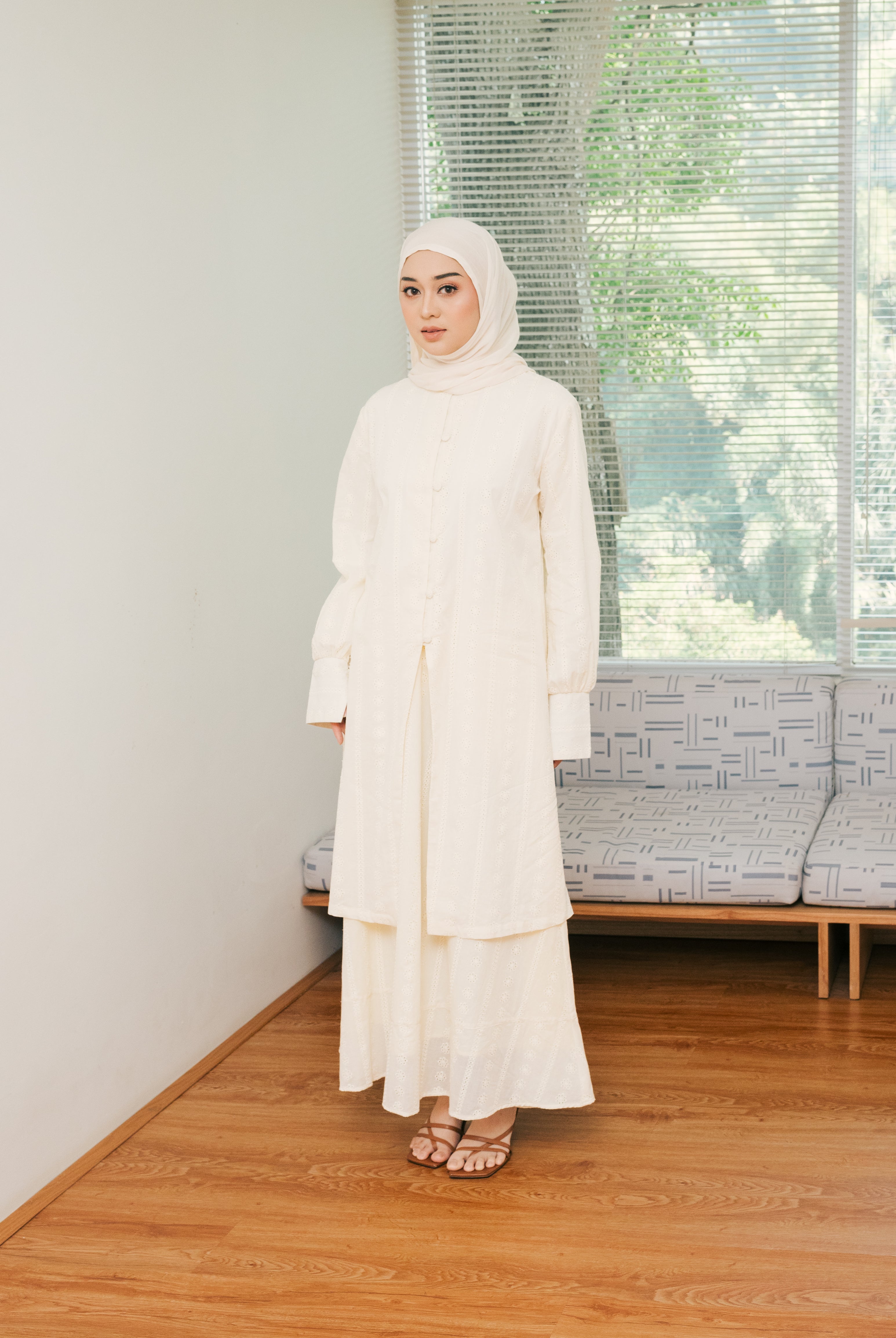 Seorang wanita memakai long embroidery tunic berbahan cotton embroidery yang premium berwarna ivory dari brand Atala Scarves, memiliki aksen yang menarik pada bagian lengan yang memiliki slit dan dilengkapi tali terpisah pada bagian pinggang.