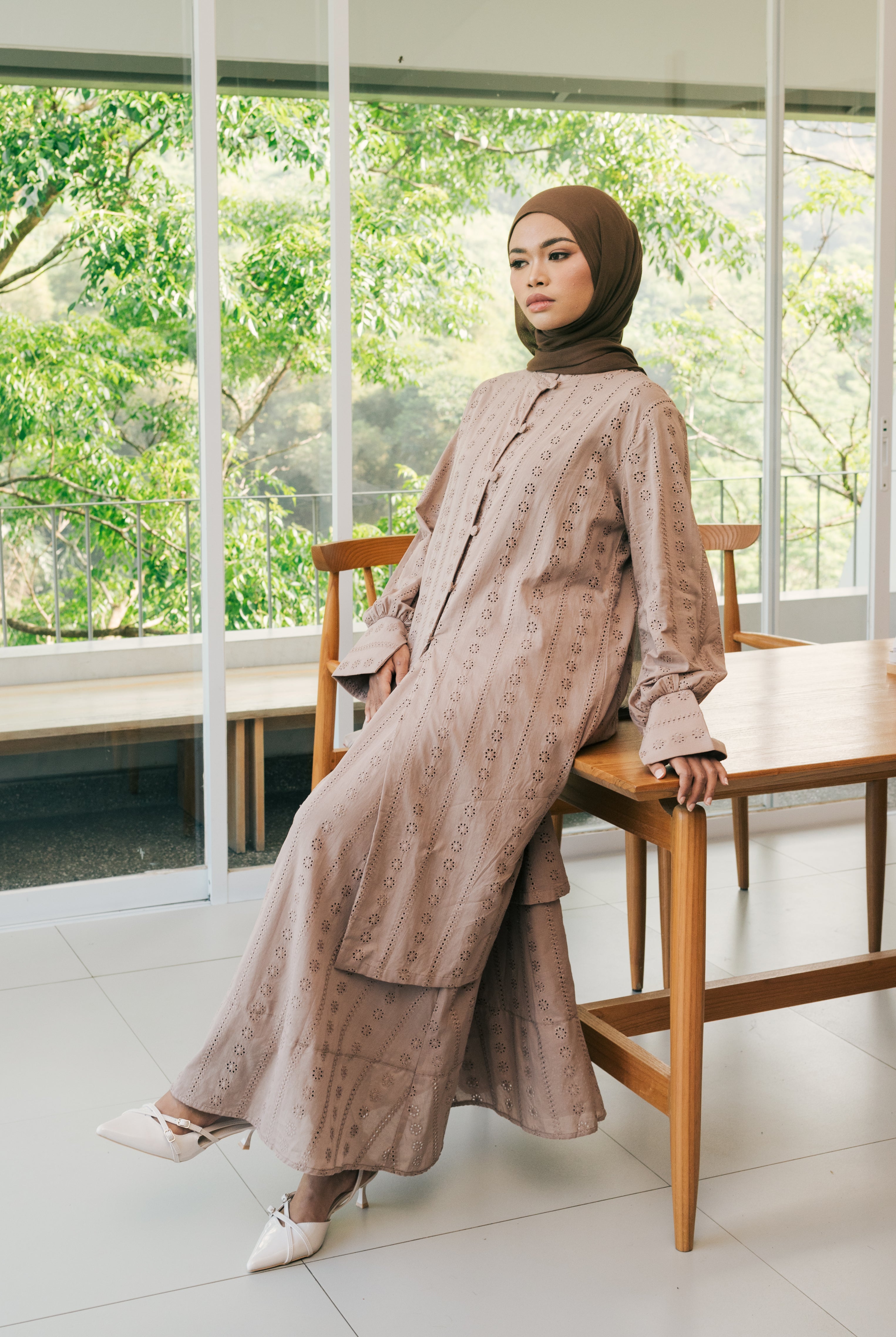 Seorang wanita memakai long embroidery tunic berbahan cotton embroidery yang premium berwarna mocca dari brand Atala Scarves, memiliki aksen yang menarik pada bagian lengan yang memiliki slit dan dilengkapi tali terpisah pada bagian pinggang.
