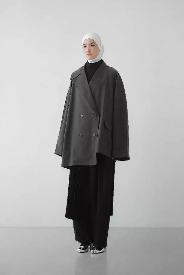 Person wearing a dark gray oversized blazer by Rashawl and black pants on a white background