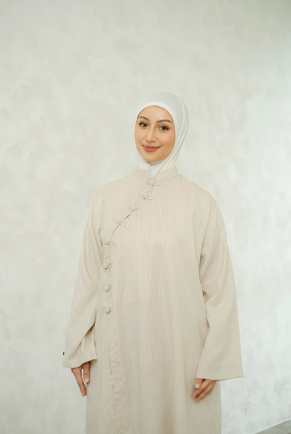Woman wearing a white hijab and ivory-colored tunic by Tufine against a white background
Seorang wanita yang mengenakan hijab putih dan tunik berwarna krem dari Tufine dengan latar belakang putih
