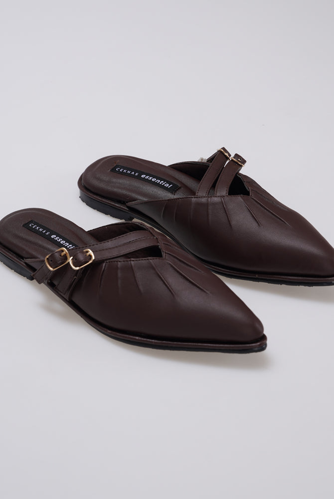 A pair of dark brown leather pointed-toe mule sandals by Cekhas with gold-tone buckle straps, shown on a light gray studio background.