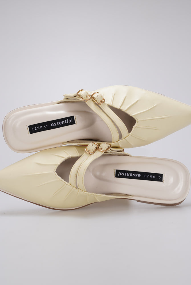 A pair of butter yellow-colored pointed-toe mule sandals by Cekhas with gold-tone hardware and a strap detail, shown from a top-down view on a light gray background.