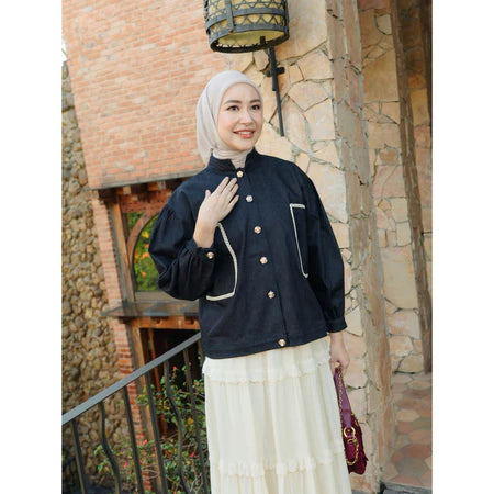 Woman wearing a dark blue jacket with white buttons from Haidee Orlin in front of a stone building.